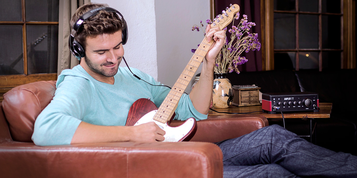 guitarist jamming on Line 6 AMPLIFi TT desktop amp modeler wearing headphones